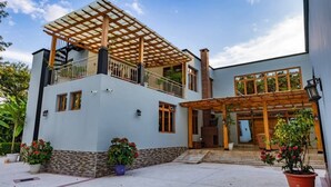 A modern two-story house with a covered patio, large windows, and potted plants.