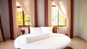 A bedroom with a large bed, curtains, and a window with a geometric pattern.