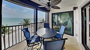 A balcony with a table and chairs, a ceiling fan, and a view of the ocean. - Seaside 403 | New Gulf-Front Condo—Your Front-Row Seat to Paradise! (Fort Myers Beach)