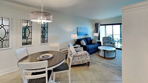 A modern living room with a dining area, featuring a round table, white chairs, a blue sofa, and patterned armchairs. - Seaside 403 | New Gulf-Front Condo—Your Front-Row Seat to Paradise! (Fort Myers Beach)