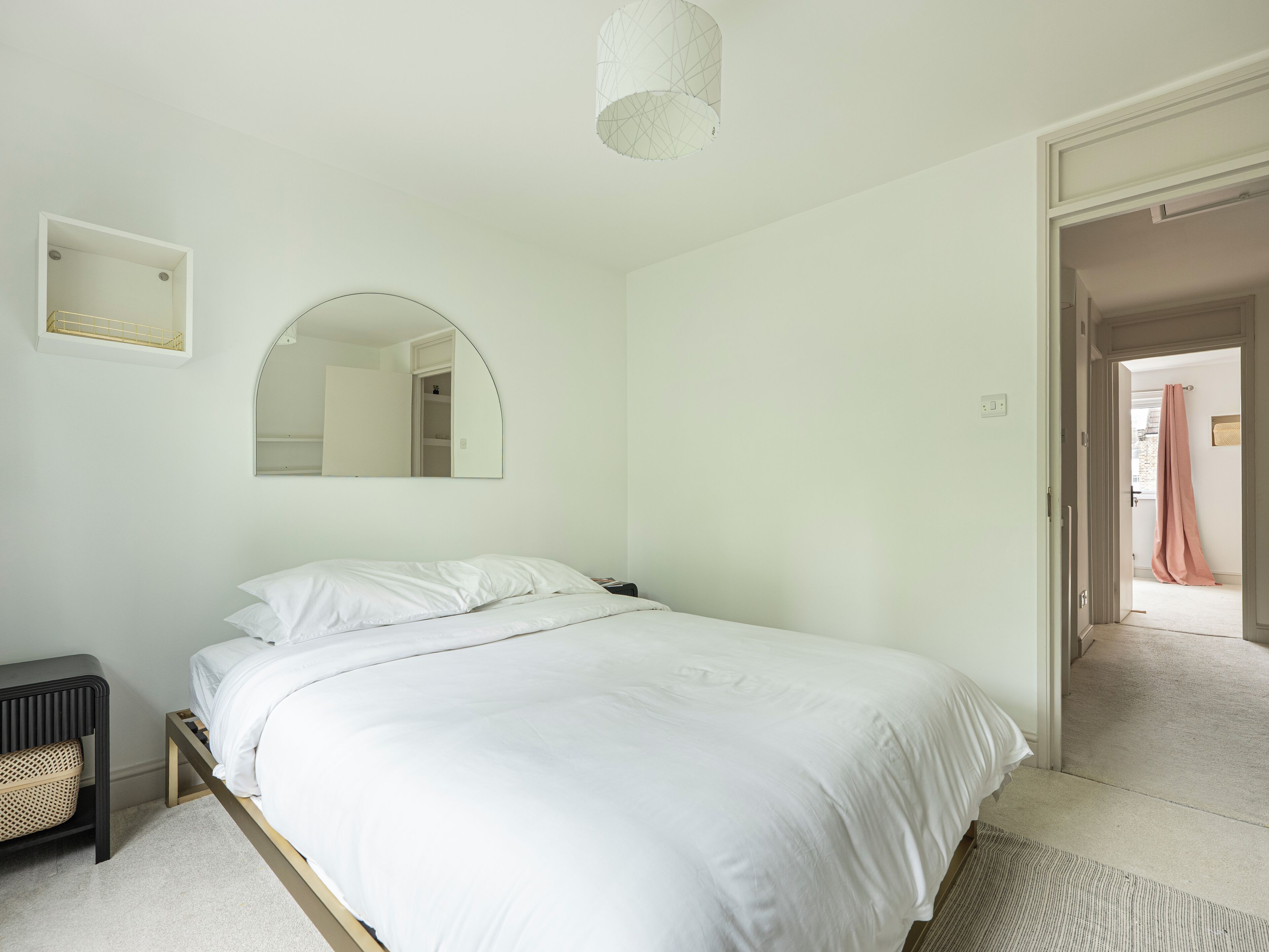 Een slaapkamer met een bed, nachtkastje, spiegel en een deur naar een andere kamer.