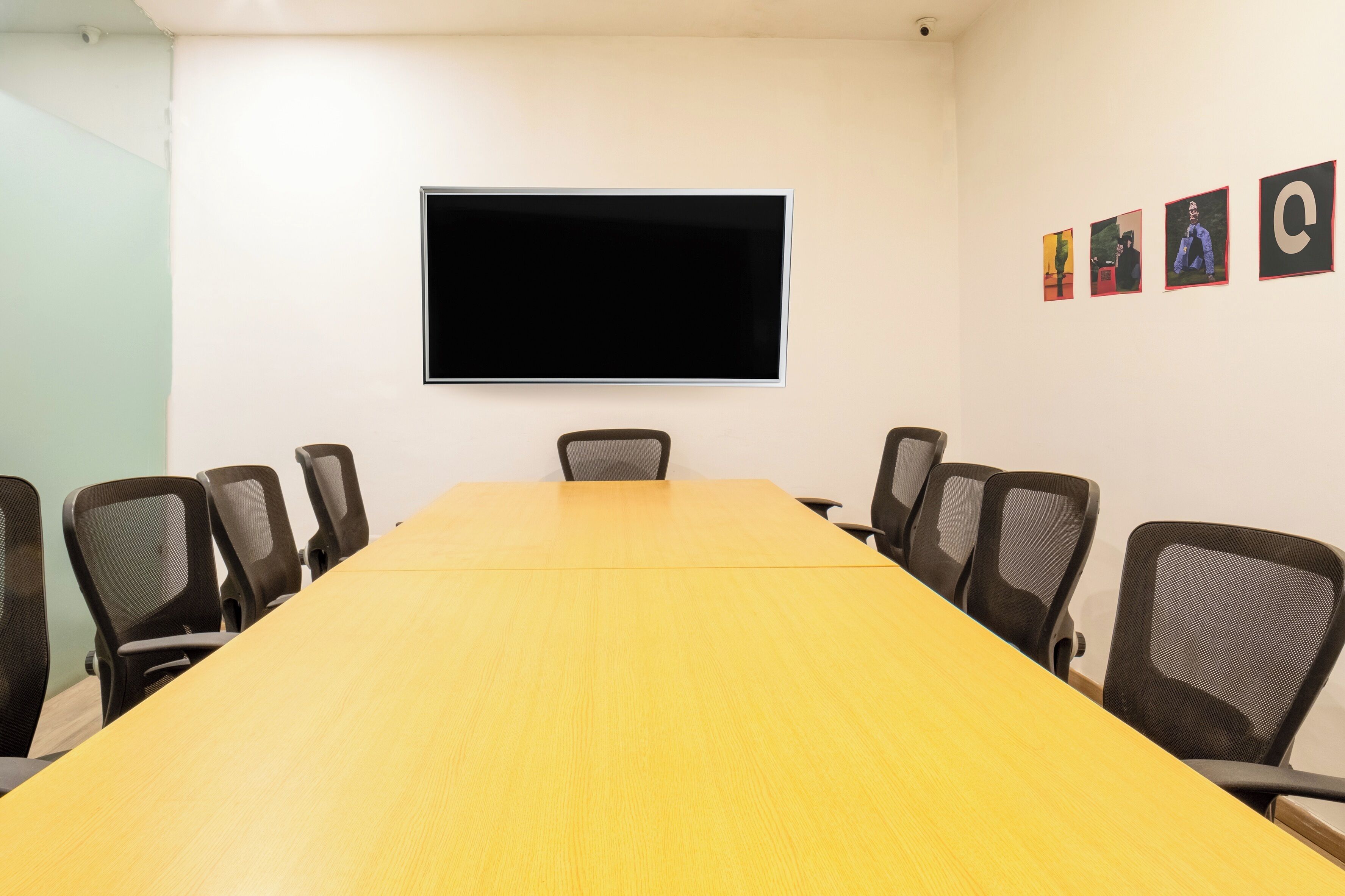 A conference room with a long table, six chairs, a flat-screen TV, and four framed pictures on the wall.