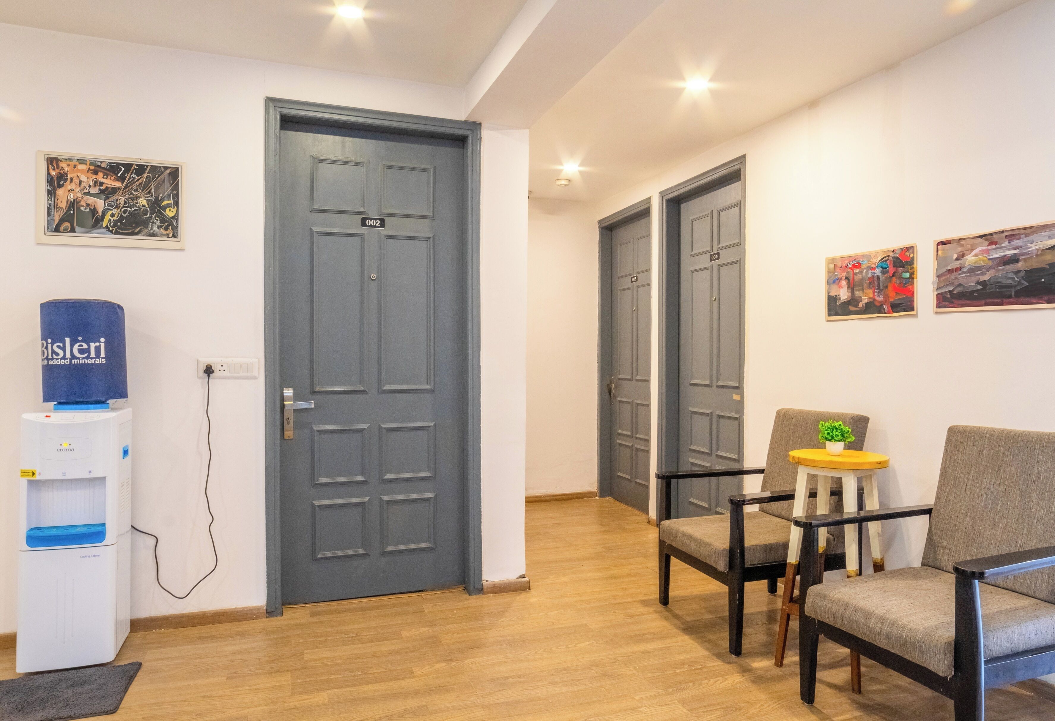 A hotel lobby with a water dispenser, two grey doors, and a seating area with chairs and a small table.