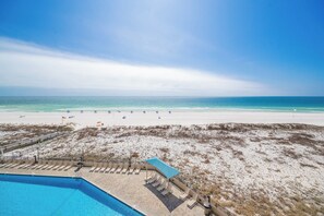 A beach view with a pool, lounge chairs, and umbrellas.