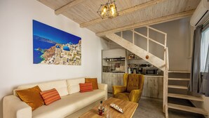 A living room with a sofa, coffee table, and a painting of a coastal village. - New Lux Misilia Suite & Prive Jacuzzi (Santorini)