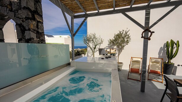 A spa area with a hot tub, seating, and a view of the sea. - New Lux Misilia Suite & Prive Jacuzzi (Santorini)