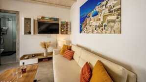 A modern living room with a beige sofa, a wooden coffee table, and a mounted TV. There is a painting of a coastal scene on the wall. - New Lux Misilia Suite & Prive Jacuzzi (Santorini)