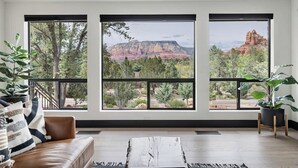 A room with a large window overlooking a mountainous landscape, a leather sofa, and a coffee table.