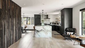 A modern kitchen with dark cabinetry, a marble island, and a dining area with a wooden table and chairs.