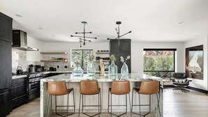 A modern kitchen with a central island, bar stools, and a dining area with a view.
