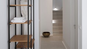 Un couloir avec une étagère en bois où sont rangées des serviettes et un bol.