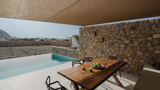 Un espace extérieur aménagé pour les repas, avec un mur en pierre, une piscine et une vue sur le paysage.