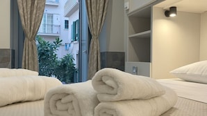 A hotel room with a bed, rolled white towels, a window with curtains, and a view of buildings and greenery outside. - CASA RUGGI COZY HOUSE 5 MINUTES FROM NAPLES CENTRAL STATION (Napoli)