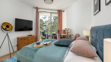 A modern bedroom with a large bed, a television, a desk, and a view of the outdoors.