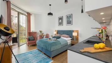 A modern hotel room with a bed, a desk, a chair, a dining table, and a kitchen area.