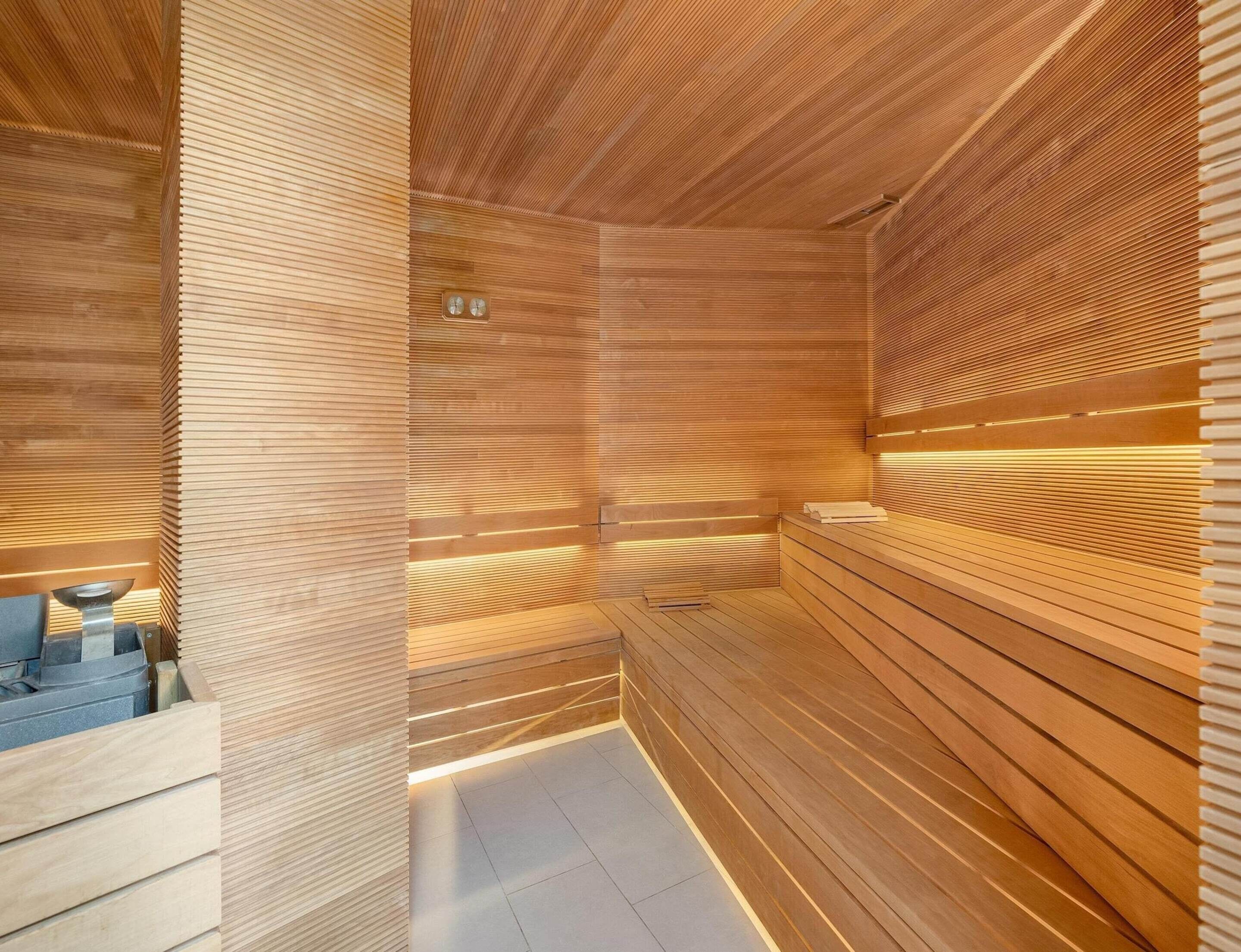 Uma sauna com ripas de madeira e um banco, uma pequena mesa com uma tigela, e um chão ladrilhado.