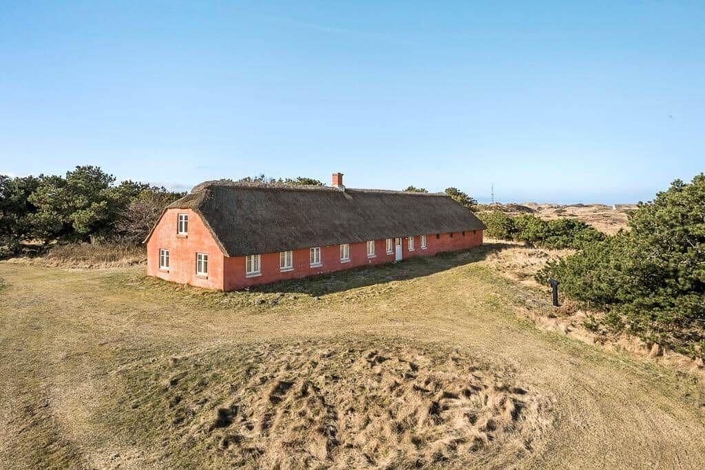 Una casa roja con techo de paja, rodeada de pasto seco y vegetación escasa.