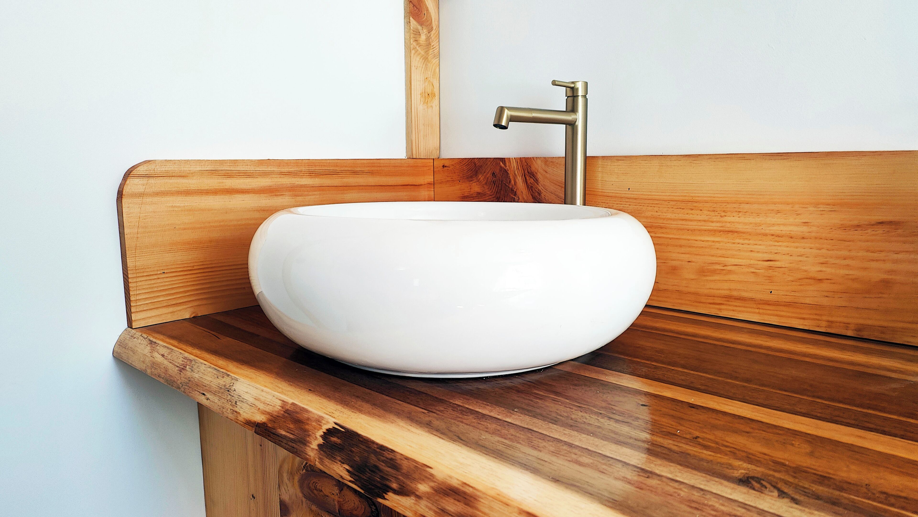 Un lavandino in ceramica bianca con un rubinetto dorato su un piano in legno.