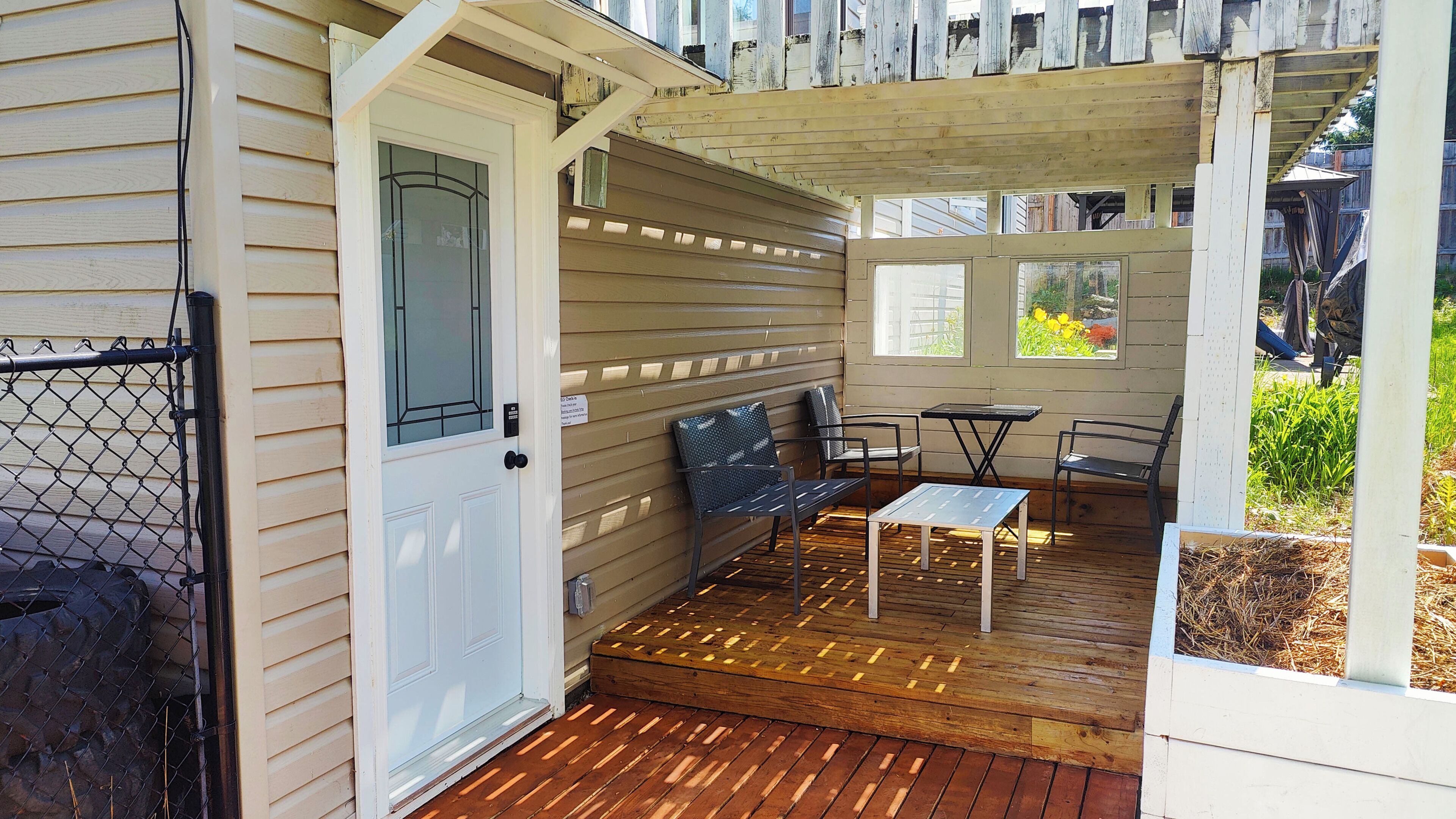 A covered porch with a wooden deck, a white door, and a seating area with two chairs and a small table.