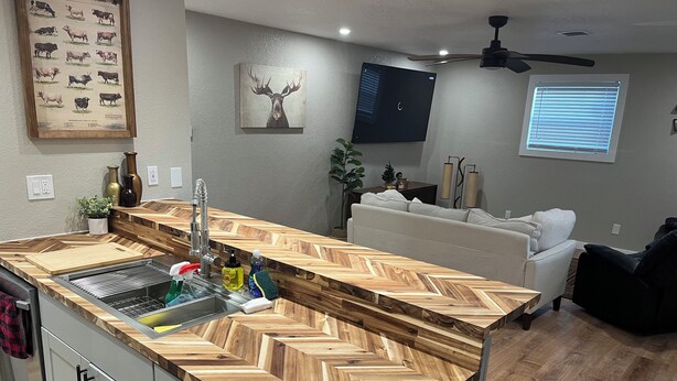 A modern kitchen with a herringbone wood countertop, a built-in sink, and a dining area with a white sofa.