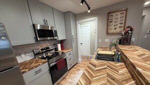 A modern kitchen with stainless steel appliances, a herringbone wood countertop, and a wooden floor.
