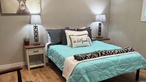 A bedroom with a teal bedspread, a deer painting on the wall, and two bedside lamps.