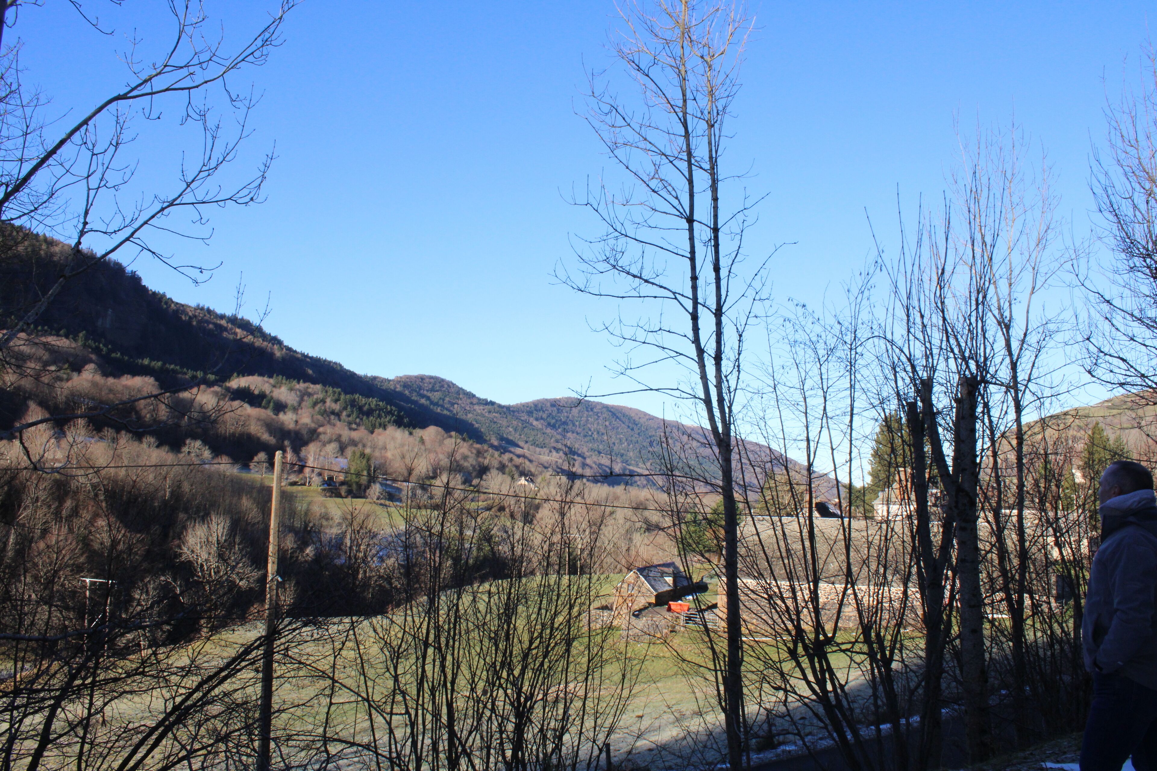 A rural landscape with a clear sky, a hilly backdrop, and a person standing in the foreground.