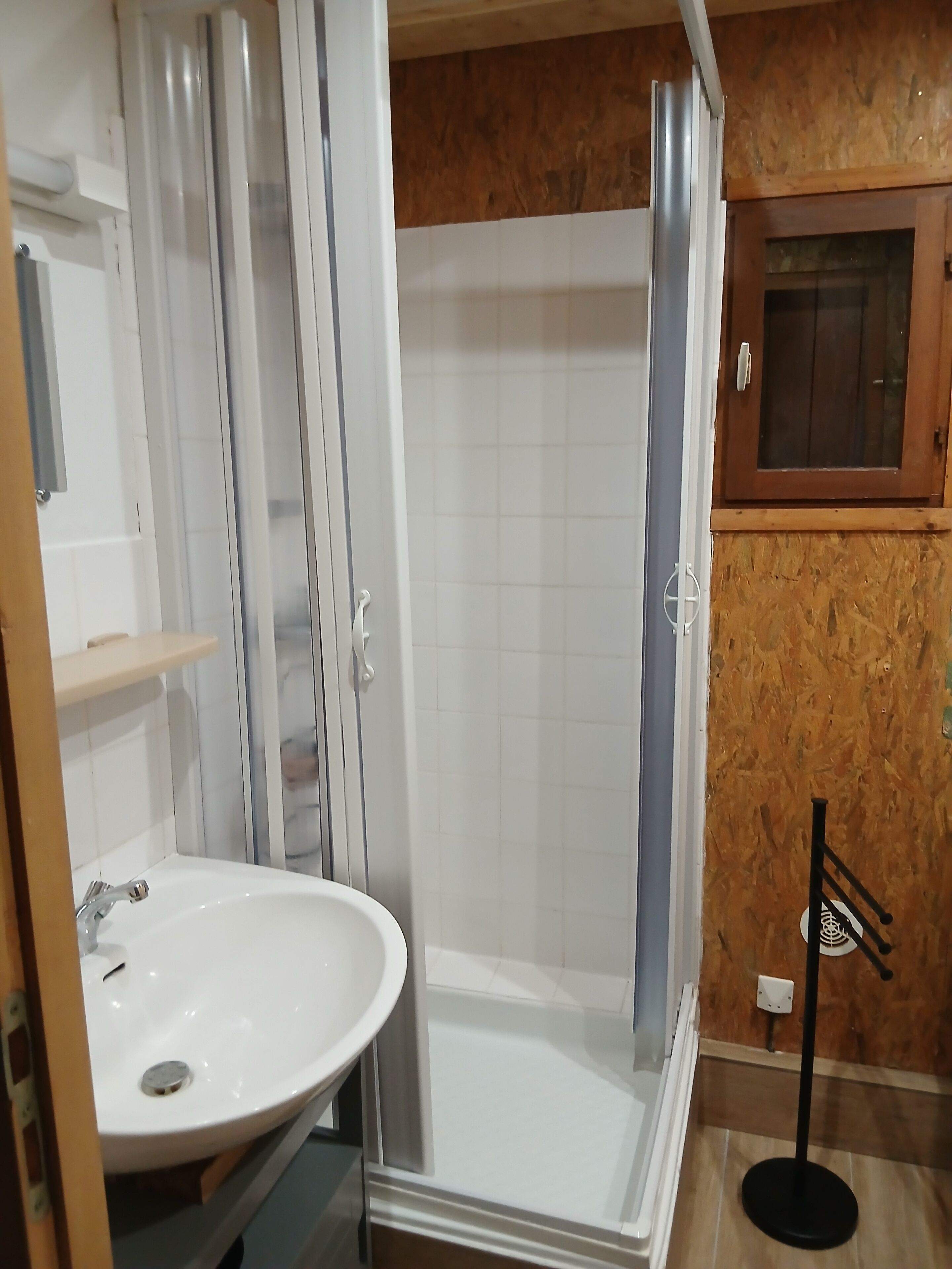 A bathroom with a white sink, a shower enclosure, and a wooden wall panel.