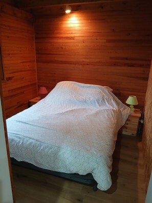 A wooden-paneled room with a bed, a nightstand, and a lamp.