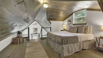 Une chambre avec un plafond en pente, un grand lit, une fenêtre avec des stores et un escalier menant à un niveau supérieur.