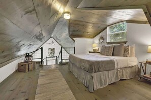 Un dormitorio con techo inclinado, una cama grande, una ventana con persianas y una escalera que sube a un nivel superior.