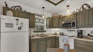 A kitchen with green cabinets, a white refrigerator, a microwave, a stove, and a sink. - Cactus Flower Lodge-Pet Friendly-Starlit Sky Views (Fredericksburg)