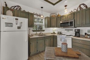 A kitchen with green cabinets, a white refrigerator, a microwave, a stove, and a sink. - Cactus Flower Lodge-Pet Friendly-Starlit Sky Views (Fredericksburg)