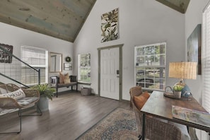 A spacious living room with a high ceiling, a staircase, and a large window with blinds. - Cactus Flower Lodge-Pet Friendly-Starlit Sky Views (Fredericksburg)