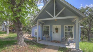 A small, single-story house with a porch, a front door, and a window with a plant. - Cactus Flower Lodge-Pet Friendly-Starlit Sky Views (Fredericksburg)