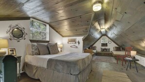 A cozy attic bedroom with a large bed, a desk, and a chair. There is a window providing natural light and a view of trees. - Cactus Flower Lodge-Pet Friendly-Starlit Sky Views (Fredericksburg)