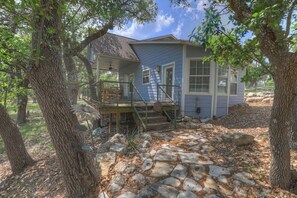 A house with a porch, stone pathway, and surrounding trees. - Cactus Flower Lodge-Pet Friendly-Starlit Sky Views (Fredericksburg)