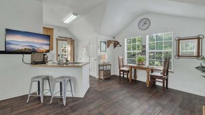 A spacious kitchen with a large island, wooden flooring, and a dining area with a view of the outdoors. - Cactus Flower Treehouse-Pet Friendly-Scenic Views! (Fredericksburg)