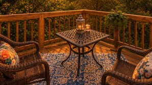 A wooden deck with wicker furniture and a table with candles, overlooking a forested landscape at sunset. - Cactus Flower Treehouse-Pet Friendly-Scenic Views! (Fredericksburg)