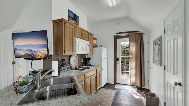 A kitchen with granite countertops, wooden cabinets, a stainless steel sink, and a microwave. - Cactus Flower Treehouse-Pet Friendly-Scenic Views! (Fredericksburg)