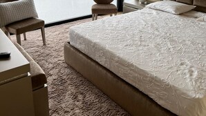 A hotel room with a large bed, a chair, a desk, and a view of a lake and hills.