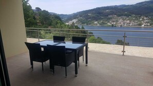 A balcony with a table and chairs overlooking a lake and hills.