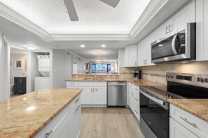 A modern kitchen with white cabinetry, granite countertops, a built-in oven, and a microwave.