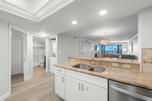 A modern kitchen with granite countertops, stainless steel appliances, and a view to the living area.