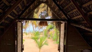 Ein offener Raum mit Holzbalkendecke und Blick auf einen Sandstrand mit Palmen.