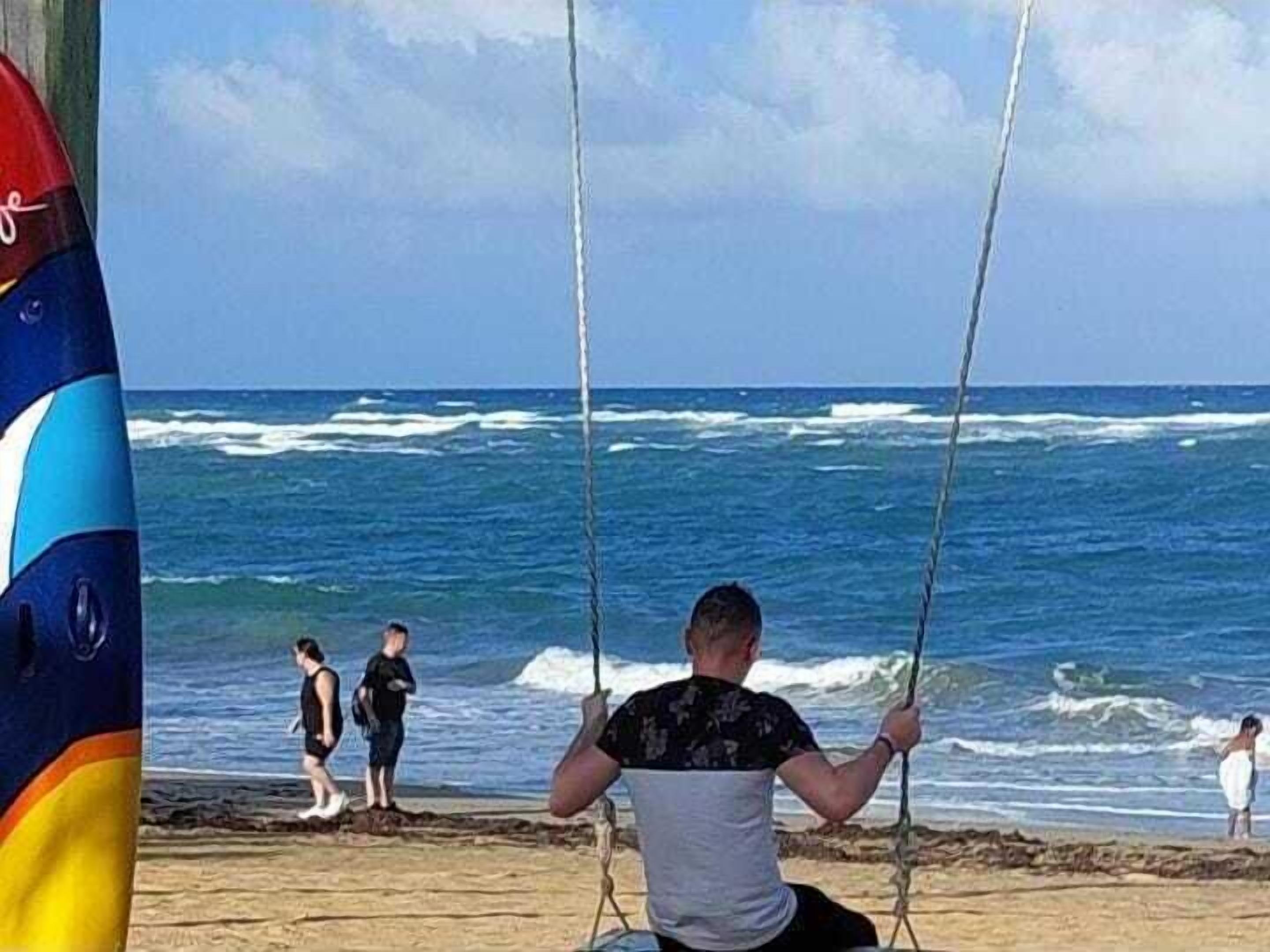 Una playa con un columpio y gente caminando por la orilla.