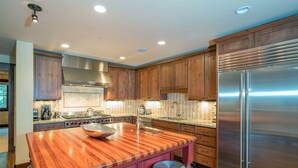 Una cocina moderna con armarios de madera, un refrigerador de acero inoxidable y una isla grande con taburetes.
