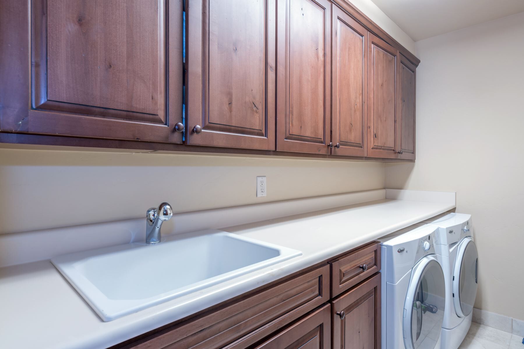 A kitchen with wooden cabinets, a white countertop, a sink, and a washing machine.