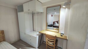 Ein Schlafzimmer mit einem Bett, einem Holztisch, einem Stuhl, einem Kleiderschrank und einem Spiegel.