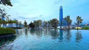 Un paisaje urbano moderno con una gran masa de agua que refleja edificios, rodeado de vegetación y palmeras.